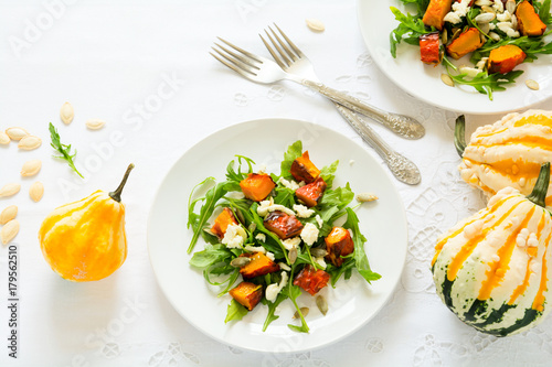 Fresh autumn salad with baked pumkin, arugula, cheese and seeds on white table cloth. Space for copy
