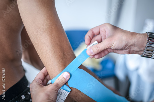 fisioterapista applica tape dopo massaggio per il dolore a un giovane sportivo 