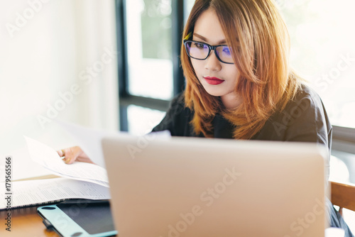 Asian stylish glasses woman designer wear black dress and red lips working with her laptop and checking the document in selective focus..