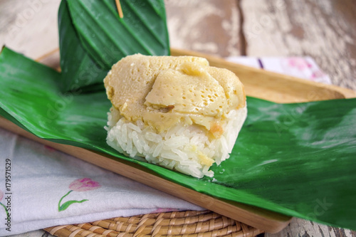 Thai dessert, sticky rice with egg custard wrap with banana leaf on wood table