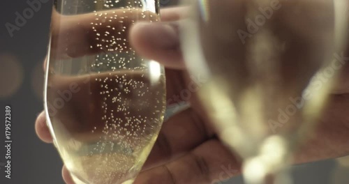 Close up of a man's hand picking up a flute glass with sparkling wine with bubbles in gray and gold tones