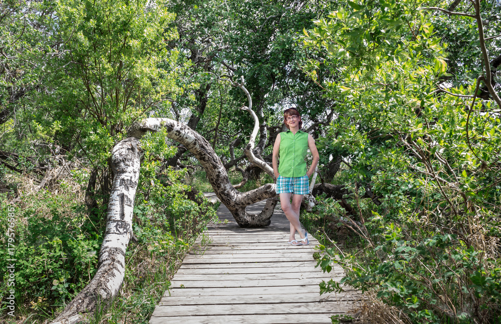 horizontal image of a caucasian woman posing on a wooden plank walk way surrounded by dense lush green trees on a warm summer day. horizontal image of a caucasian woman posing on a wooden plank walk way surrounded by dense lush green trees on a warm summer day.