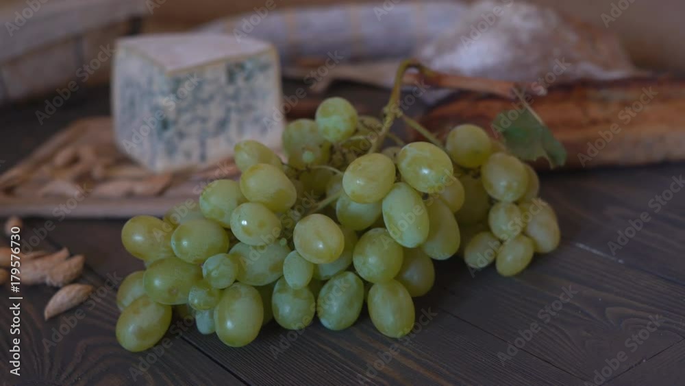 panoramic shooting from the slider. on a brown wooden table lies the green cheese quarter of the head. bread of different varieties of their dark flour. in the background grapes, and cutlery fork and panoramic shooting from the slider. on a brown wooden table lies the green cheese quarter of the head. bread of different varieties of their dark flour. in the background grapes, and cutlery fork and