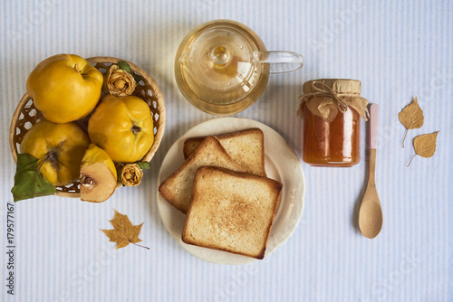 Jar of homemade jam with tea, sandwich and quinces on white background