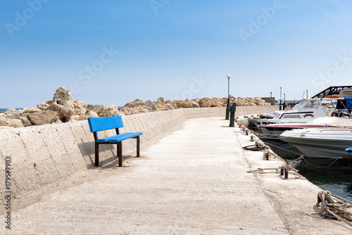 Small promenade with blue bench in small fishing port of Faliraki town on Rhodes island, Greece.
