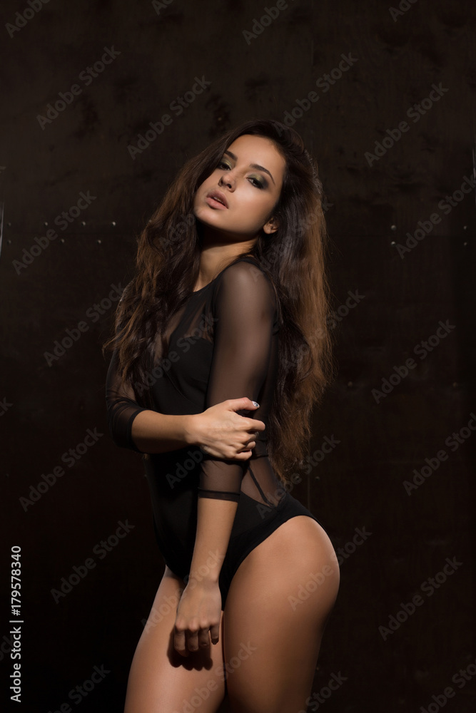 Amazing young model with athletic body in sexy lingerie posing near dark wall