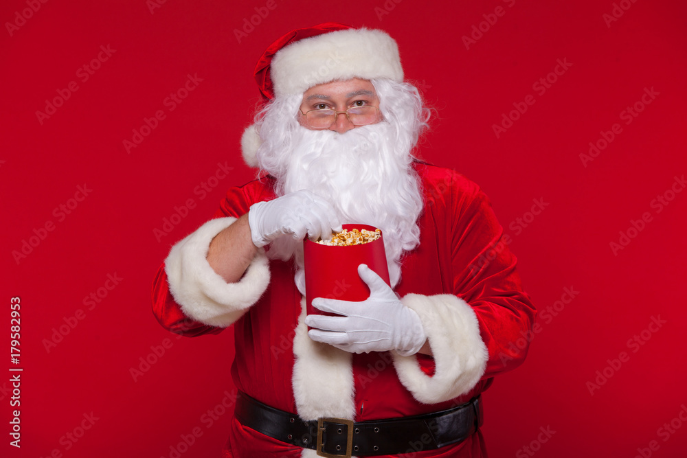 Traditional Santa Claus watching TV, eating popcorn. Christmas. Red background. emotions fear surprise