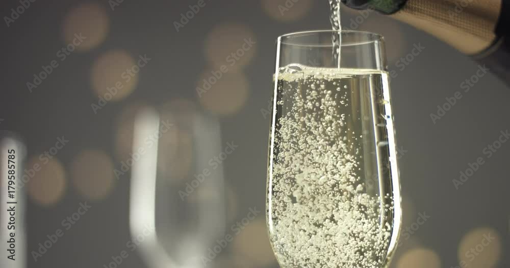 Close up video of pouring sparkling wine into a chilled glass on gray backround with blurred lights