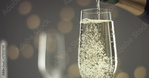 Close up video of pouring sparkling wine into a chilled glass on gray backround with blurred lights