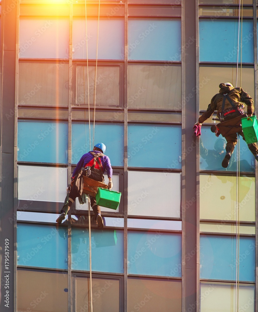 Person hanging on a rope washing windows of office building Person hanging on a rope washing windows of office building