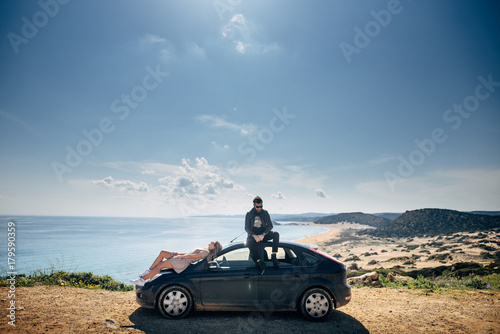 Couple sitting on a car, sea and mountain on background