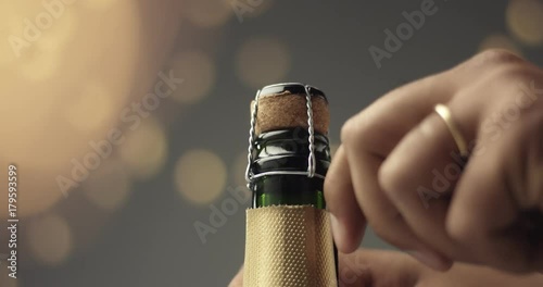Close up video of man's hands opening a bottle of champagne on gray background with lights and flares