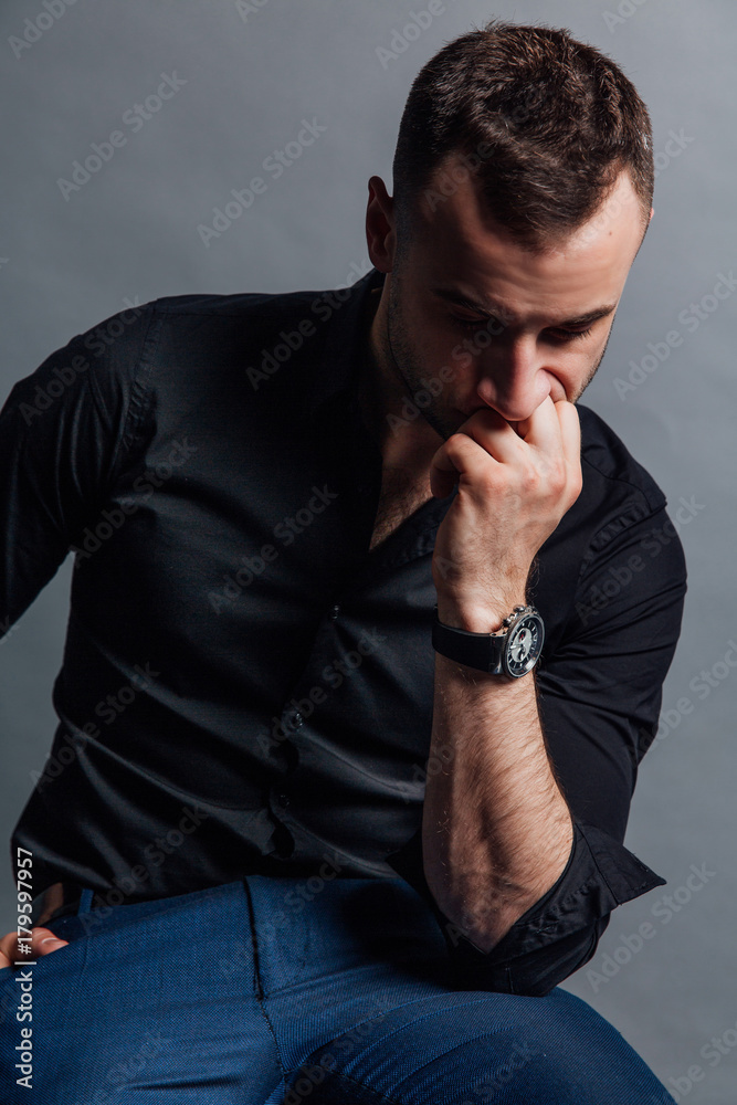 Portrait handsome fashionable man in a black shirt sits on a chair in a photo studio loft. Portrait handsome fashionable man in a black shirt sits on a chair in a photo studio loft.
