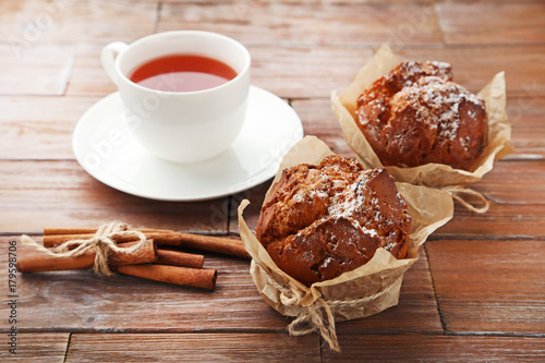 Tasty muffins with cinnamon and cup of tea on brown wooden table