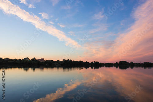 Summer countryside landscape with river. Beautiful clouds reflected in water. Colorful sunset cloudy sky