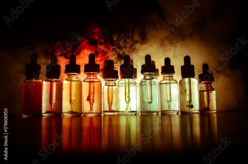 Vape concept. Smoke clouds and vape liquid bottles on dark background. Light effects. Useful as background or vape advertisement or vape background. Selective focus