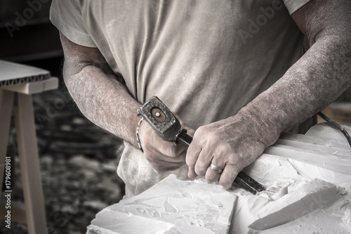 Particolare delle mani dell'artista che lavora il marmo con martello e scalpello photo