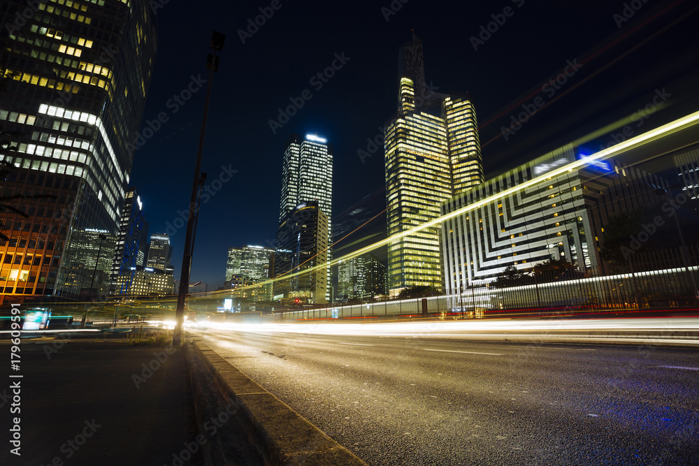Skyscrapers in Paris business district La Defense. European night cityscape with dynamic street traffic, car lights and glass facades of modern buildings. Economy, finances, transport concept. Toned