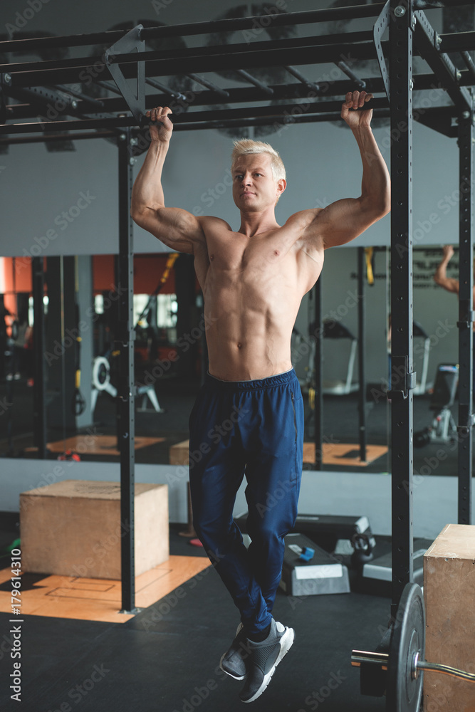 Fototapeta premium Muscular athlete man making Pull-up in gym. Bodybuilder training in fitness club showing his perfect back and shoulder muscles. Toned image