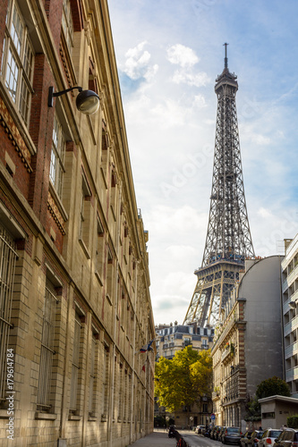 View from an adjacent street of the majestic Eiffel Tower in its immediate neighborhood with typical parisian buildings in the foreground.
