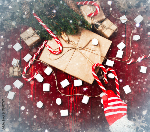 Christmas composition, concept of new year. Boxes of surprises, candy staff, rope, Christmas tree branches, bumps, marshmelow on wooden mahogany background. Hand using candy draws gift.  painted snow photo