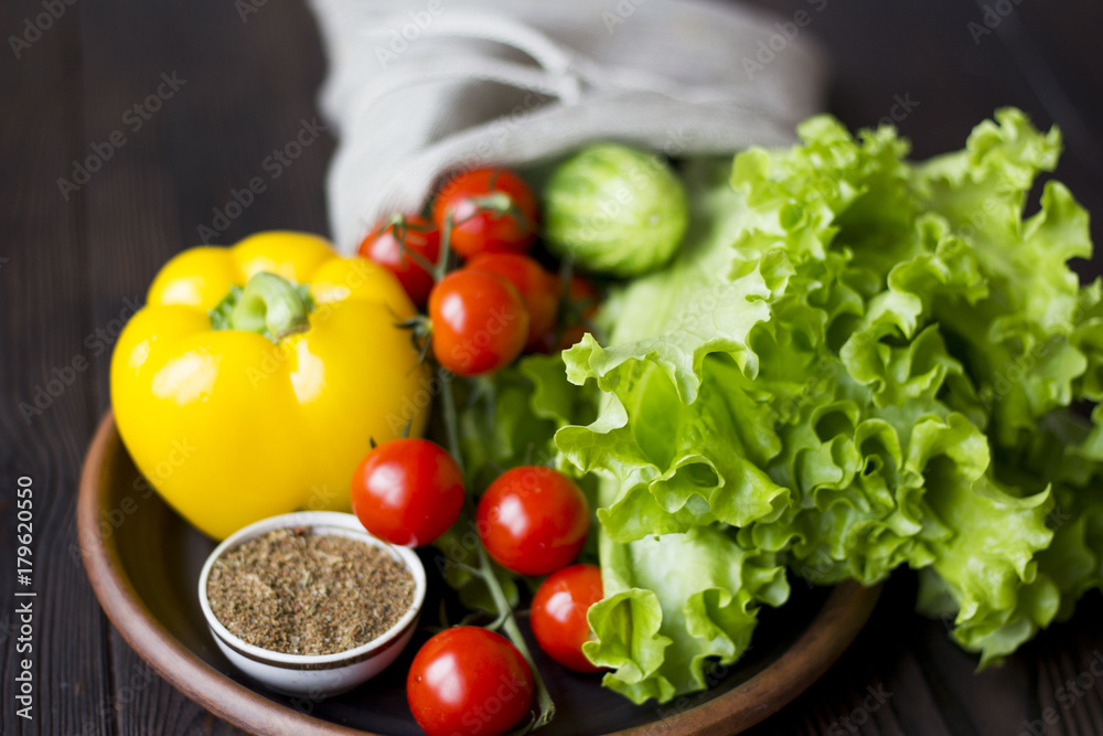 fresh organic vegetables: tomatoes, peppers, cucumber, chili, spices and salad in a clay plate on the table dark wood