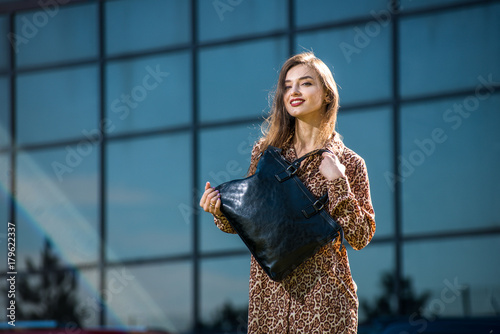 beautiful young woman posing with a leather bag in a dress