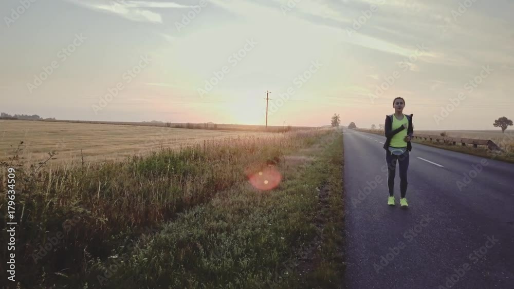AERIAL 4K: Woman Running on a Countryside Road at Sunrise. Drone shot of a Female jogger athlete training at dusk. Active healthy lifestyle concept. Cinematic morning sports footage. AERIAL 4K: Woman Running on a Countryside Road at Sunrise. Drone shot of a Female jogger athlete training at dusk. Active healthy lifestyle concept. Cinematic morning sports footage.