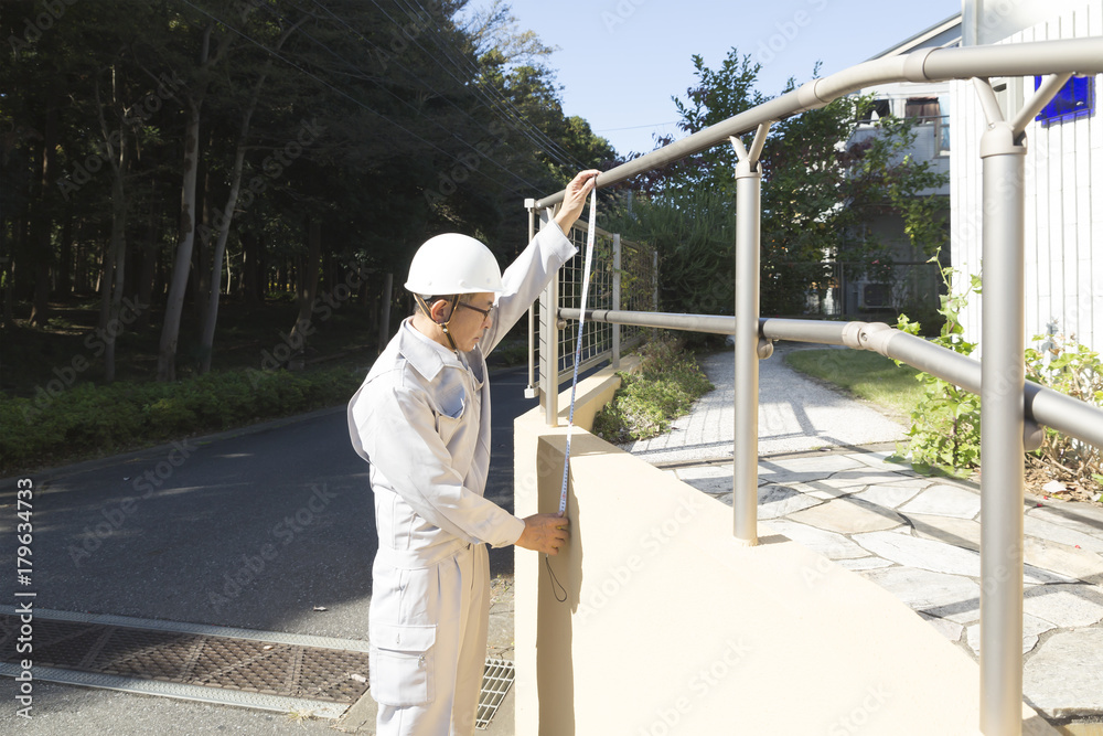 住宅 ヘルメット男性 汎用素材 メジャーでフェンス外構を採寸 住宅 ヘルメット男性 汎用素材 メジャーでフェンス外構を採寸