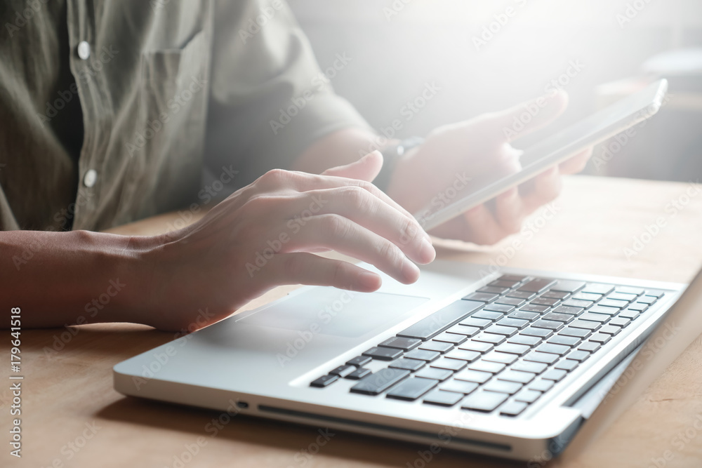 Close up of Male hands using laptop and tablet on the table, toned with sunlight Close up of Male hands using laptop and tablet on the table, toned with sunlight