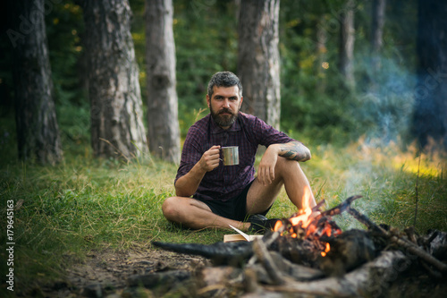 Hipster hiker with mug relax at bonfire in forest