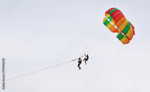 People are enjoy parasailing water sport. Fly with colorful parachute on the sky over the beach.