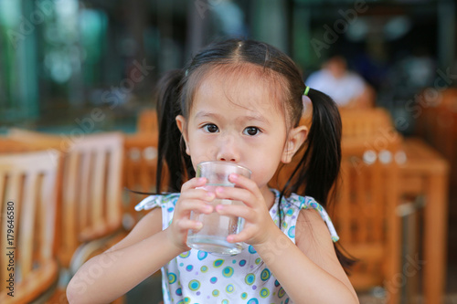 Asian little girl is drinking a water from glass with looking at camera.