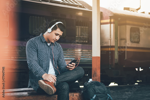 Hipster asian man listen music at train station.
