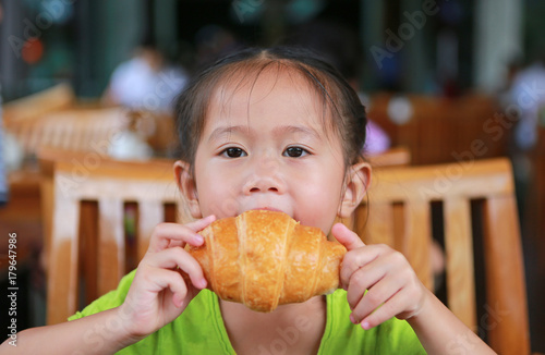 Cute little girl eating croissant at restaurant.