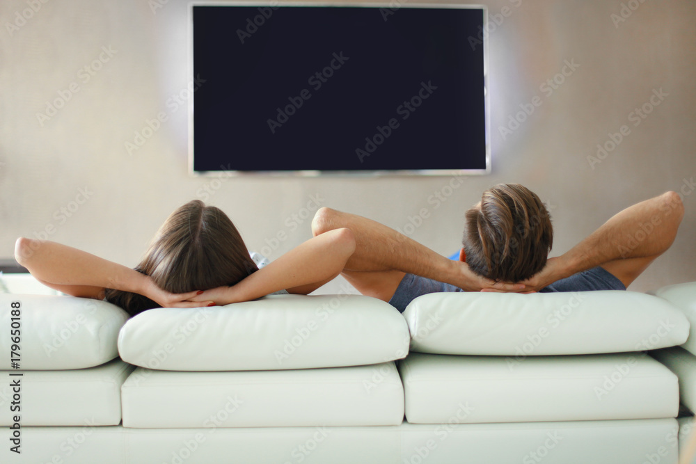 Φωτογραφία Rear view of a couple relaxing on a sofa and watching TV at home.