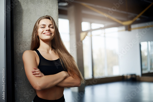 Portrait of adult fitness coach lady looking at camera with empty gym on background. Fit body concept.