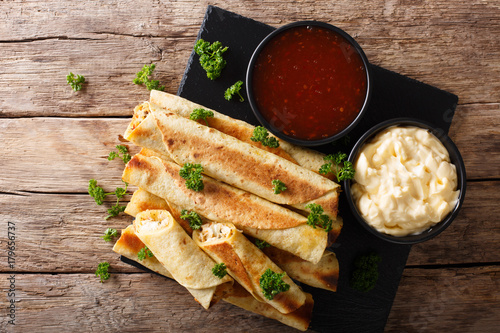 Mexican taquitos with chicken and cheese stuffing close-up, and sauces. Horizontal top view photo