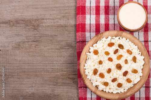 Cottage cheese in bowl with sour cream and raisins on old wooden background with copy space for your text. Top view