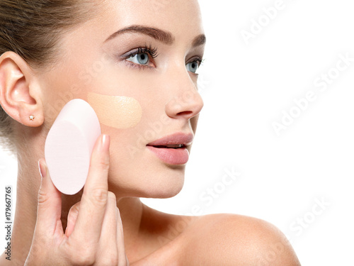 Foto Girl applies  tonal foundation  on the face use sponge