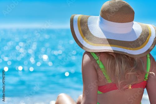 Woman in bonnet hat sitting on the ground and looking at the sea. Back view. © Artem