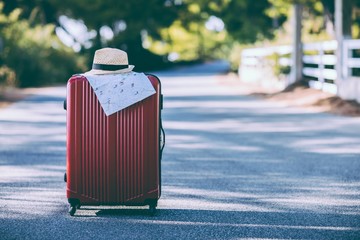 Red suitcase, hat and map on the road in countryside. Vacation and travel concept