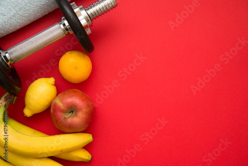 Losing weight concept with dumbbell, towel, lemon, tangerine, apple on red background