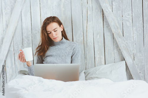 young blogger or business woman working at home with social media, drinking coffee in early morning in bed. Modern living in scandinavian interior, casual lifestyle photo