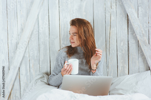 young blogger or business woman working at home with social media, drinking coffee in early morning in bed. Modern living in scandinavian interior, casual lifestyle photo