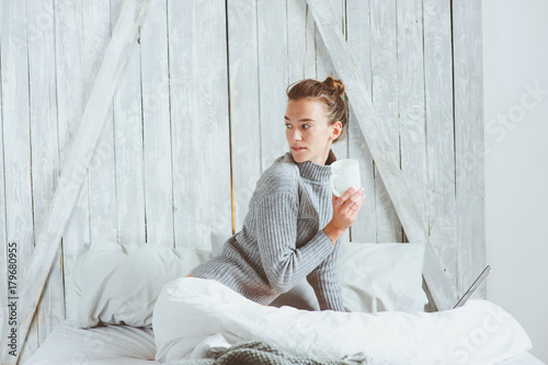 young blogger or business woman working at home with social media, drinking coffee in early morning in bed. Modern living in scandinavian interior, casual lifestyle photo