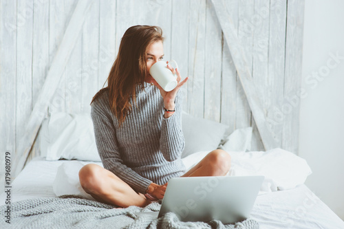 young blogger woman working at home with social media, drinking coffee in early morning in bed. Modern living in scandinavian interior, casual lifestyle photo