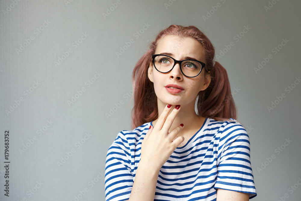 Thoughts, ideas and contemplation concept. Headshot of thoughtful upset pink haired teenage girl facing problems at school, looking up and raising eyebrows, her grimace expressing frustration