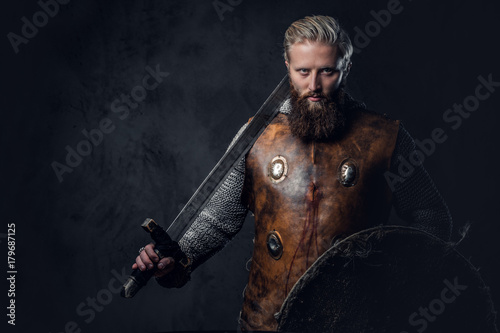 Viking dressed in Nordic armor holds a shield and silver sword.