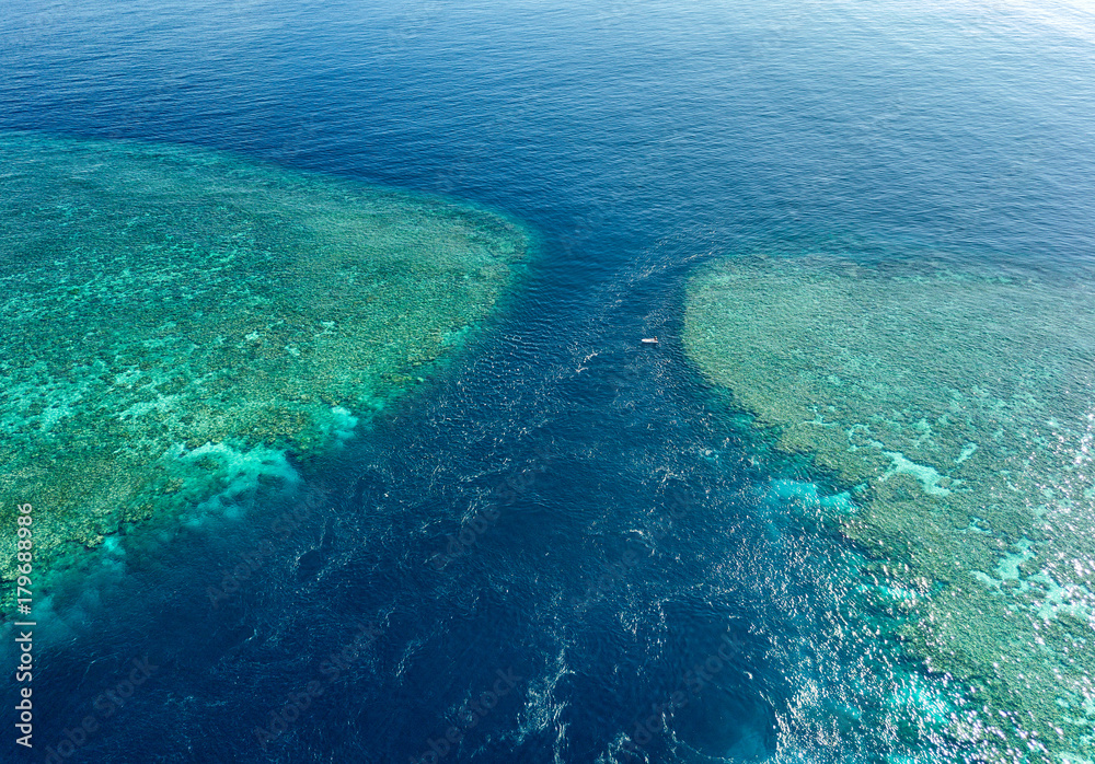 Aerial view of the Great Barrier Reef with a small boat between 2 reefs with a lot of current